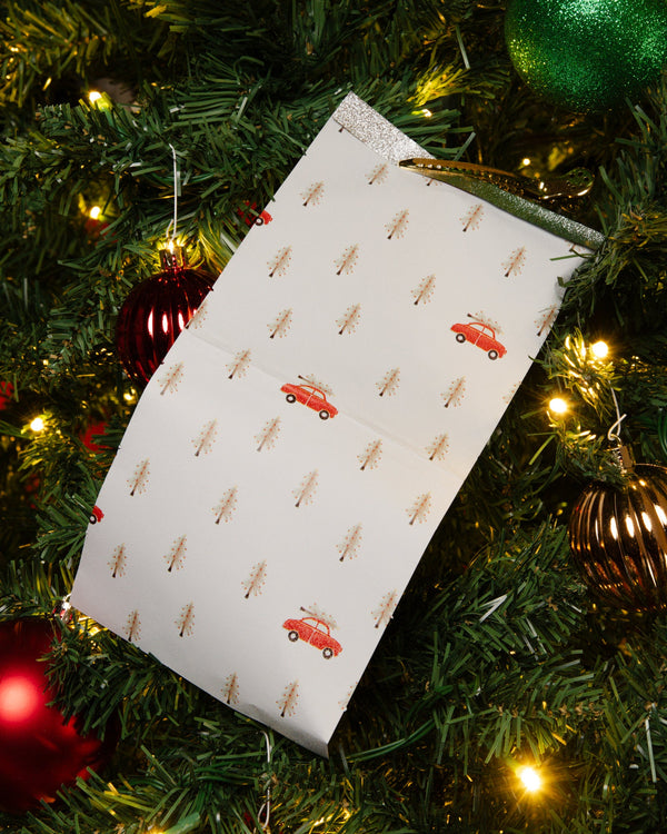 A sheet of Holly Days foil printed with tiny gold trees and red trucks, hanging in a lit Christmas tree